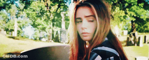 Young Woman With Red Hair Sitting In Cemetery Eyes Closed GIF
