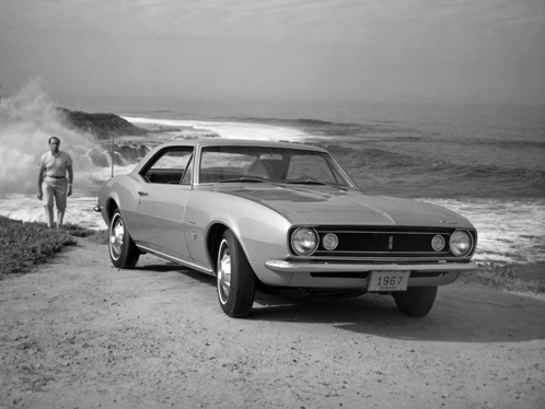 A 1967 Chevy Camaro Is Parked On A Dirt Road Near The Ocean GIF