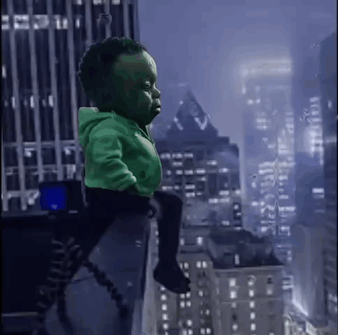 a baby dressed as the hulk is sitting on a person 's shoulders in front of a city skyline .