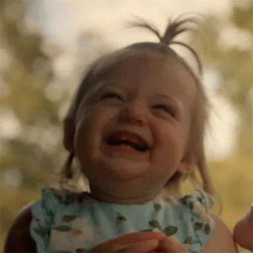 A Baby Girl In A Blue Dress Is Laughing With Her Mouth Open GIF