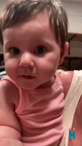 A Baby Girl In A Pink Tank Top Is Being Held By A Woman GIF
