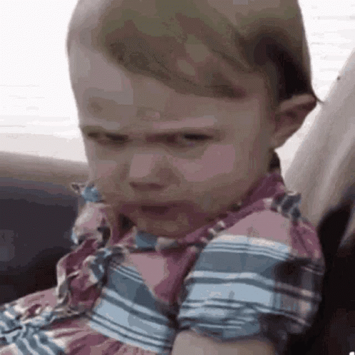 A Baby Girl Is Making A Funny Face While Sitting On A Couch . GIF
