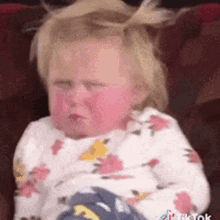 A Baby Girl Is Sitting On A Couch With Her Eyes Closed And Making A Sad Face . GIF