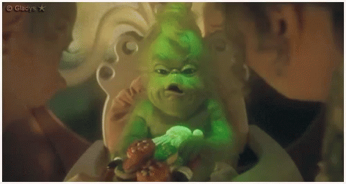A Baby Grinch Is Sitting In A High Chair With A Candy Cane . GIF