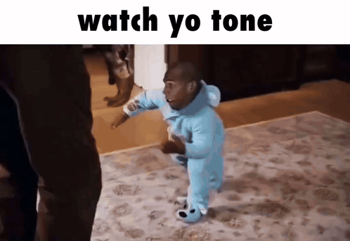 A Baby In A Blue Onesie Is Walking On A Rug With The Words " Watch Yo Tone " Above Him GIF