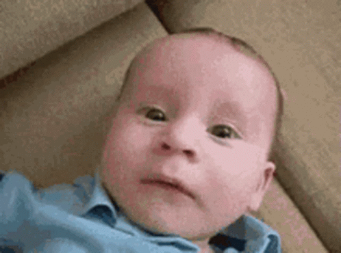 A Baby In A Blue Shirt Is Laying On A Couch And Making A Funny Face . GIF