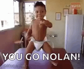 A Baby In A Diaper Is Pointing At The Camera While Standing On A Purple Balloon . GIF