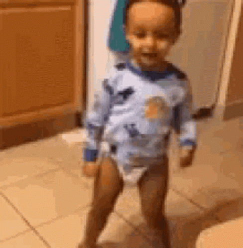 A Baby In A Diaper Is Standing On A Tiled Floor In A Room . GIF