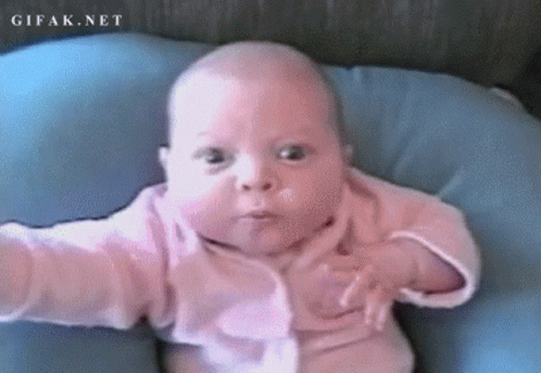 a baby in a pink shirt is laying on a blue pillow with gifak.net written on the bottom right