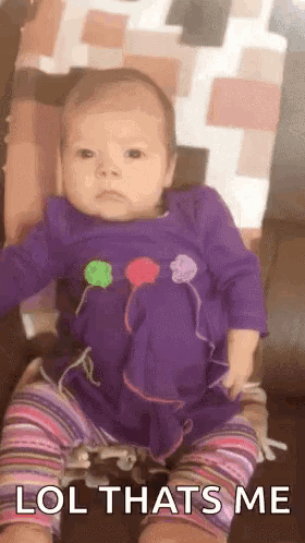 A Baby In A Purple Dress Is Sitting On A Couch And Making A Face . GIF
