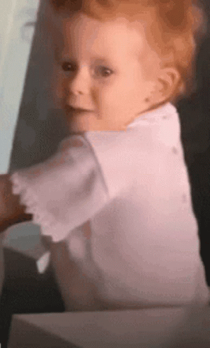 A Baby In A White Shirt Looks At The Camera GIF