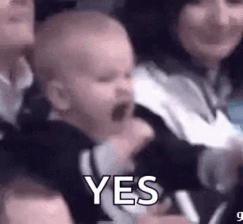 A Baby Is Being Held By A Woman In A Crowd And Making A Funny Face . GIF