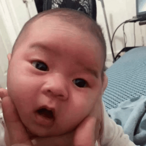 A Baby Is Being Held In Someone 'S Arms And Making A Surprised Face . GIF