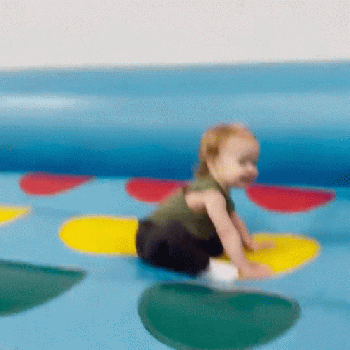 A Baby Is Crawling On A Colorful Twister Toy GIF