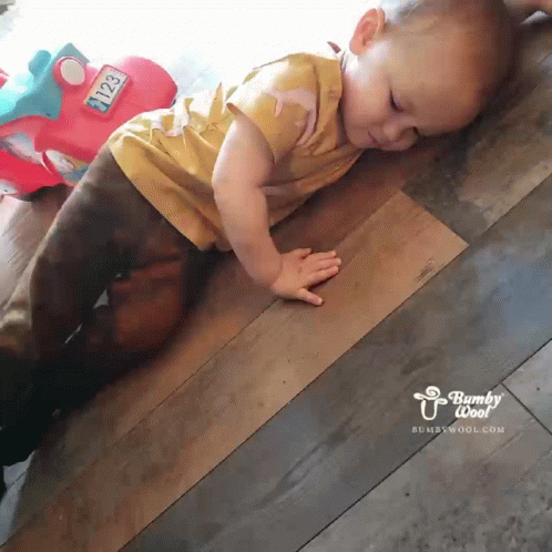 A Baby Is Crawling On A Wooden Floor Next To A Toy Car With The Number 2123 On It GIF