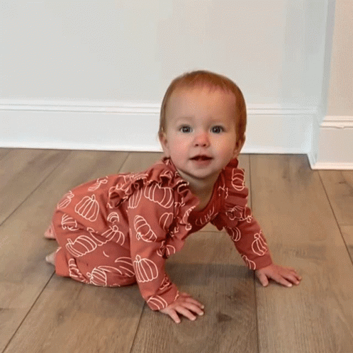 A Baby Is Crawling On A Wooden Floor Wearing A Pink Outfit With Pumpkins On It GIF