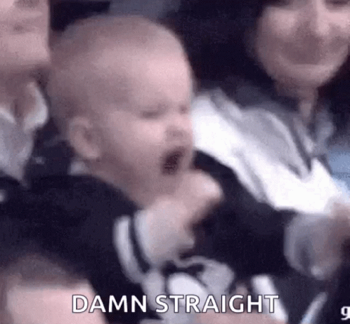 A Baby Is Crying In A Crowd Of People While A Woman Holds It . GIF