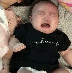 A Baby Is Crying While Being Held By A Woman And Wearing A Black Shirt . GIF