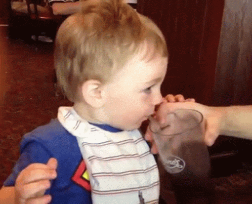 A Baby Is Drinking From A Glass With The Word Ford On It GIF