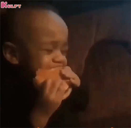 a baby is eating a hamburger in a dark room while a woman looks on .