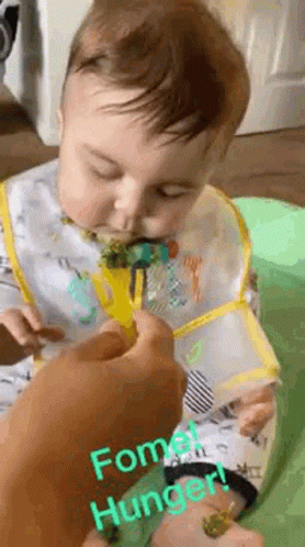 A Baby Is Eating Broccoli With A Fork And Bib On . GIF