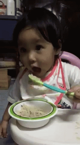 A Baby Is Eating From A Bowl With A Spoon In It GIF