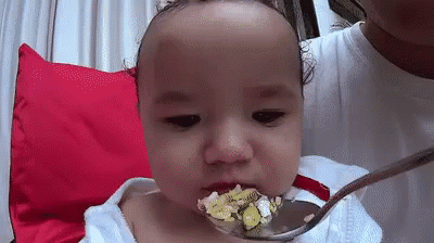 A Baby Is Eating From A Spoon With A Spoon In His Mouth . GIF