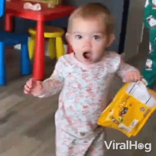 A Baby Is Holding A Bag Of Chips In Her Hands . GIF