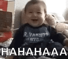 A Baby Is Laughing While Sitting On A Bed With Boxes . GIF