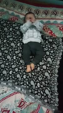A Baby Is Laying On A Bed With A Paisley Patterned Blanket GIF
