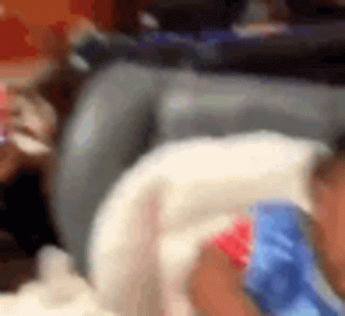 A Baby Is Laying On A Couch Wearing A Blue And Red Shirt . GIF
