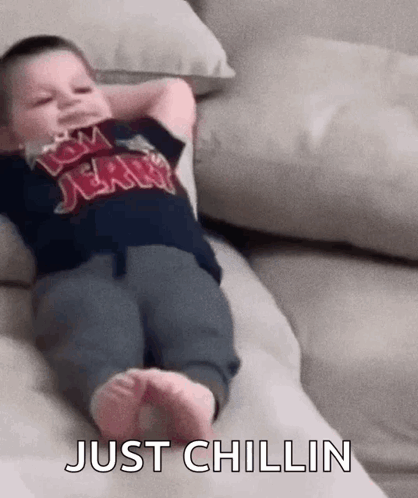 A Baby Is Laying On A Couch With His Arms Over His Head And The Words `` Just Chillin '' Written On The Bottom . GIF