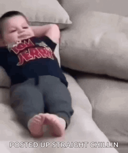 A Baby Is Laying On A Couch With His Hands Behind His Head And His Feet Up . GIF