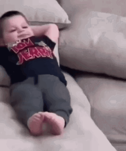 A Baby Is Laying On A Couch With His Hands Behind His Head And Wearing A Tom And Jerry Shirt . GIF
