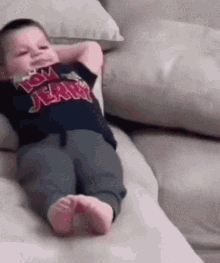 A Baby Is Laying On A Couch With His Hands Behind His Head And Wearing A Tom Jerry Shirt . GIF