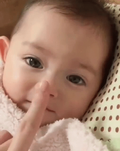 A Baby Is Laying On A Polka Dot Pillow And Touching His Nose . GIF