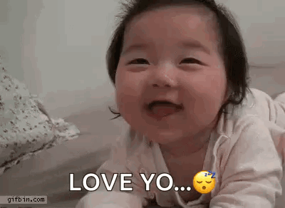 A Baby Is Laying On Its Stomach And Smiling While Saying `` Love You '' . GIF