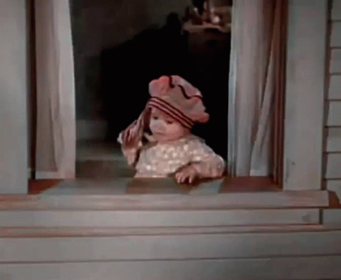 A Baby Is Looking Out Of A Window Wearing A Hat And Holding A Towel . GIF