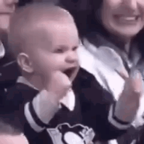 A Baby Is Making A Fist In The Air While Sitting Next To A Woman . GIF