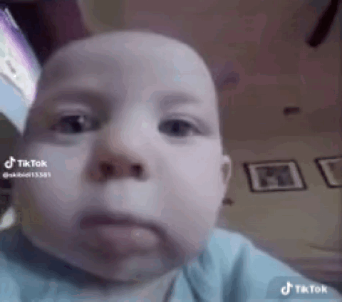 A Baby Is Making A Funny Face While Looking At The Camera In A Living Room . GIF