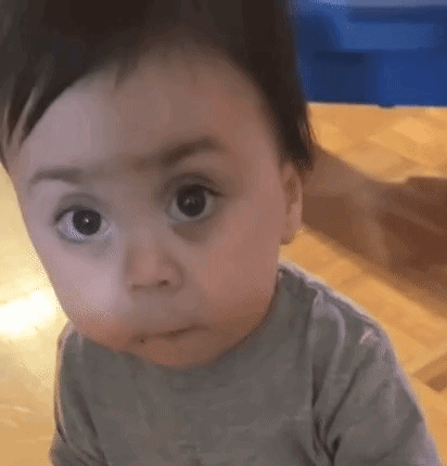 A Baby Is Making A Funny Face While Sitting On The Floor . GIF