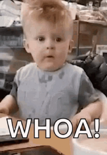 A Baby Is Sitting At A Table And Making A Funny Face While Wearing A Bib And Saying `` Whoa ! '' GIF