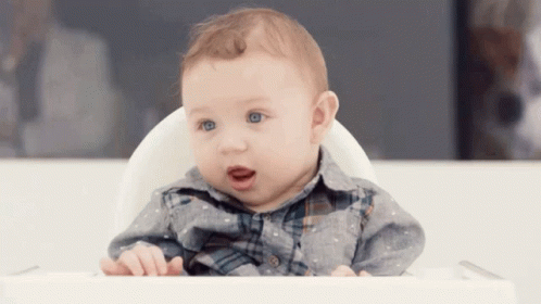 A Baby Is Sitting In A High Chair And Looking At The Camera GIF