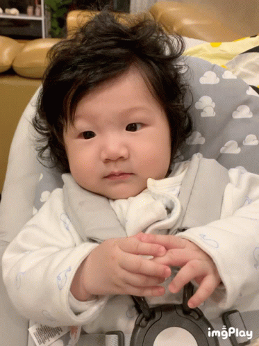 A Baby Is Sitting In A High Chair With A Cloudy Pillow GIF