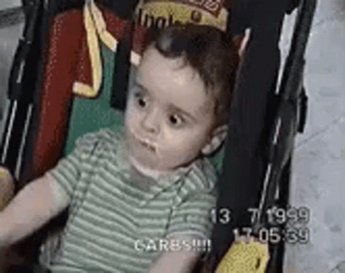 A Baby Is Sitting In A Stroller With A Crown On His Head . GIF