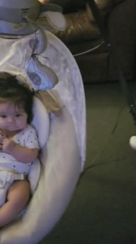 A Baby Is Sitting In A Swing With A White Cover On It GIF