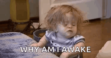 A Baby Is Sitting On A Couch With His Eyes Closed And A Blanket On The Floor . GIF