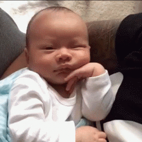 A Baby Is Sitting On A Couch With His Hand On His Face . GIF