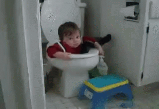 A Baby Is Sitting On A Toilet With A Broom In His Hand . GIF