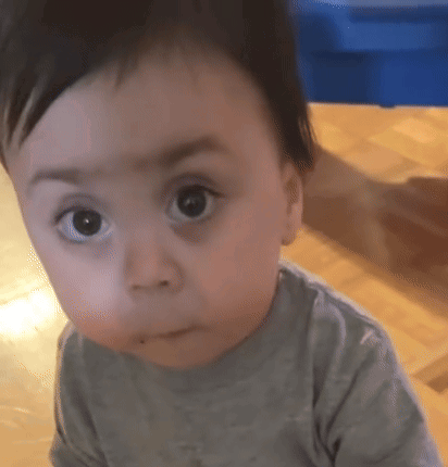 A Baby Is Sitting On A Wooden Floor And Making A Funny Face GIF